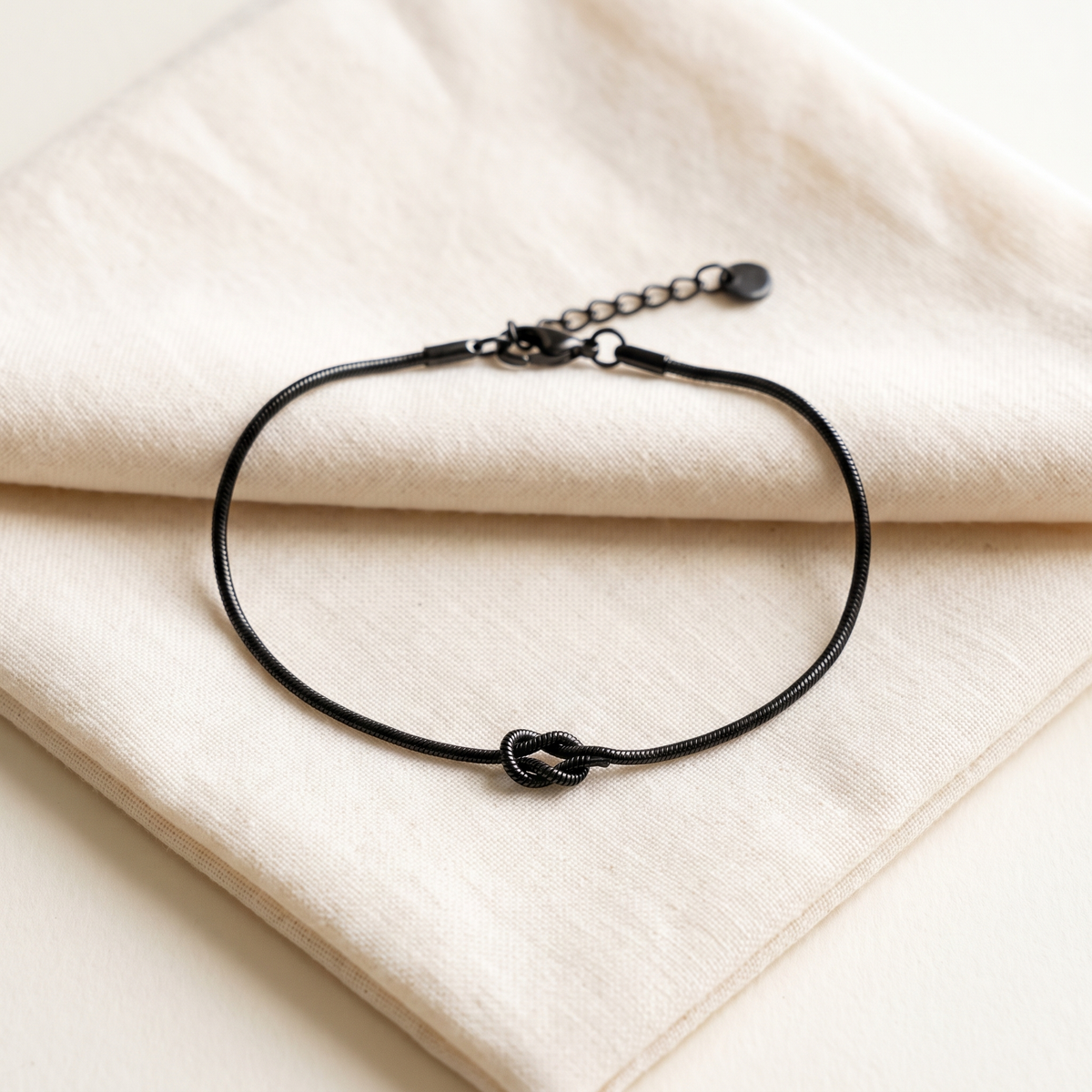 The matte black Forever Knot bracelet open on cream cotton