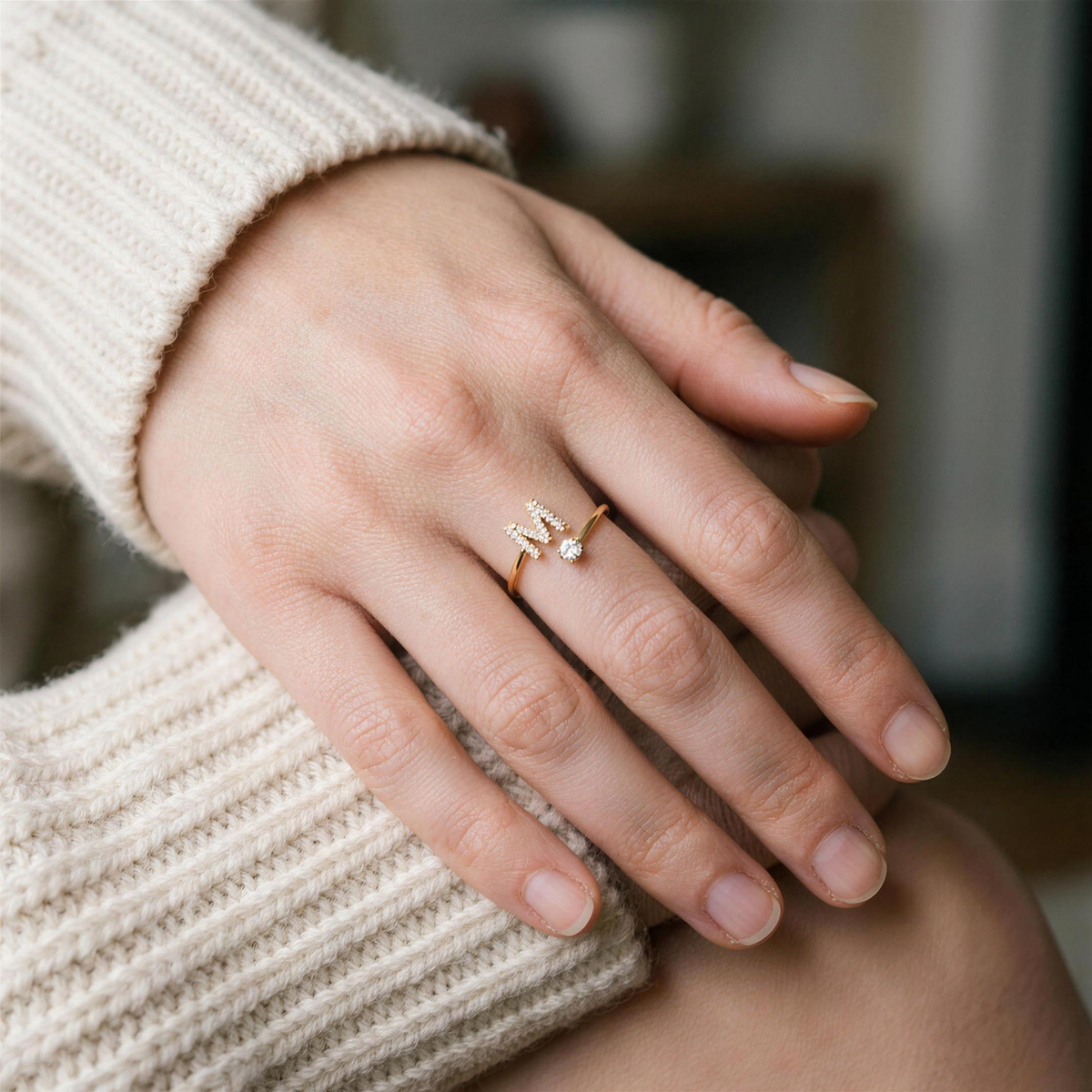 Gold initial ring with a paved letter M worn on the ring finger, hand resting on a cream knit sweater