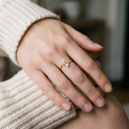 Gold initial ring with a paved letter M worn on the ring finger, hand resting on a cream knit sweater