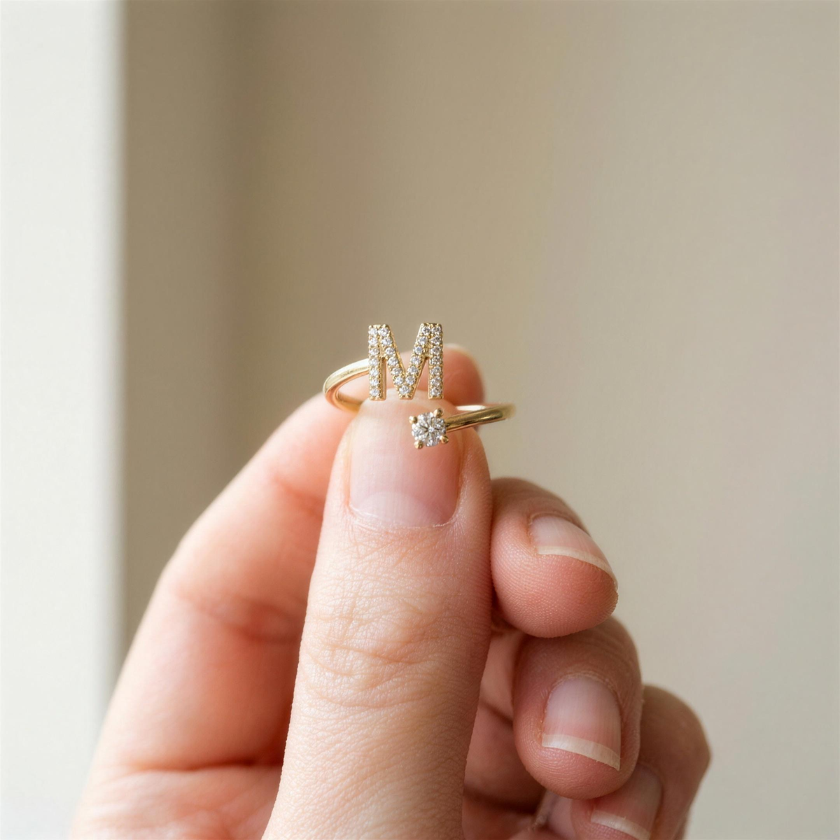 Gold initial ring with a paved letter M held between two fingertips