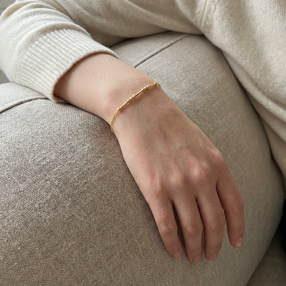 The gold Morse code bracelet worn, her hand resting on the sofa