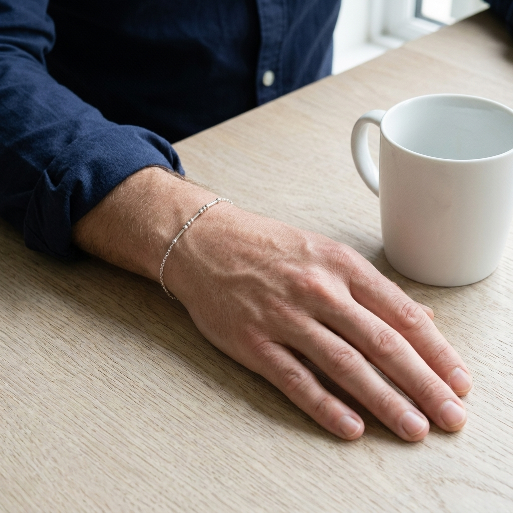 The silver Morse code bracelet on a man's wrist next to a mug