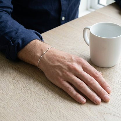 The silver Morse code bracelet on a man's wrist next to a mug