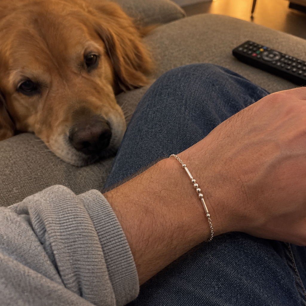 The silver Morse code bracelet on his wrist, his dog beside him on the sofa