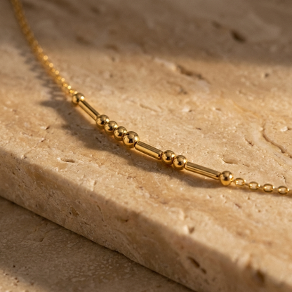 Close-up of the round gold beads and slim gold bars on the fine cable chain