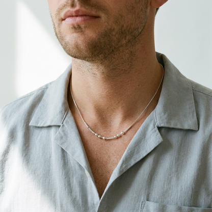 The silver Morse code necklace worn by a man in an open shirt