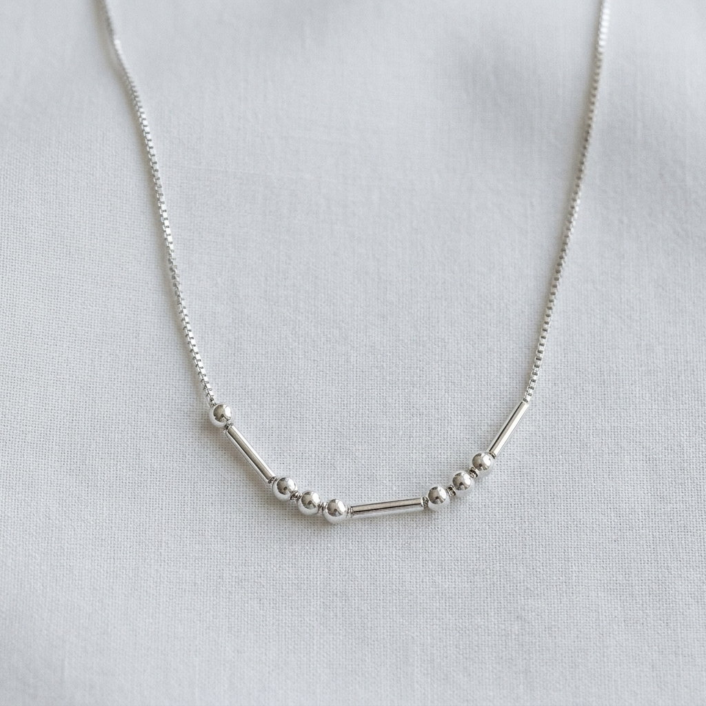 The silver Morse code necklace on pale linen