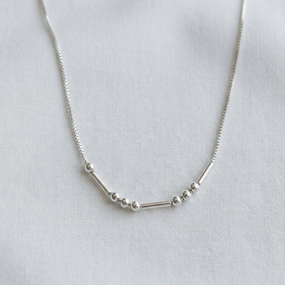 The silver Morse code necklace on pale linen