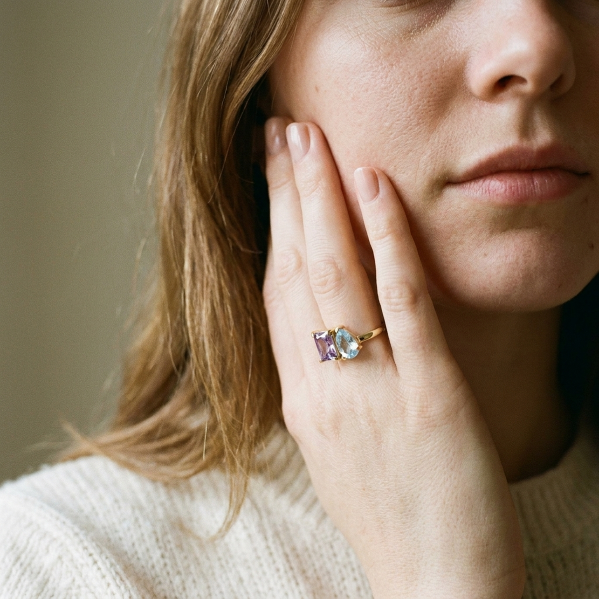 A woman's hand against her cheek wearing the two-birthstone gold ring