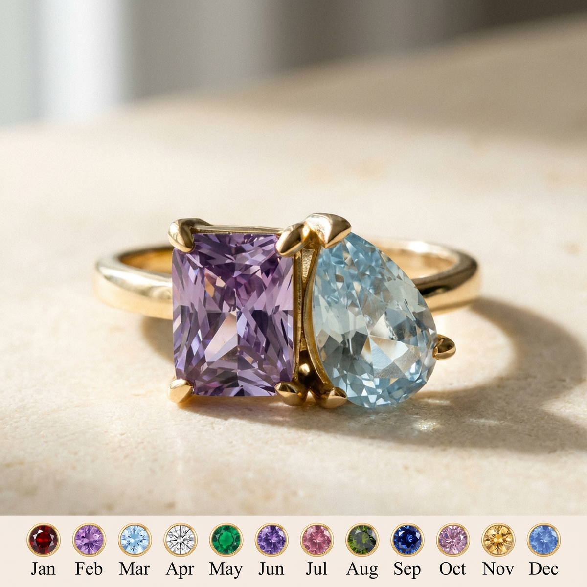 Gold ring with a purple radiant-cut stone and a light blue pear-cut stone on cream stone