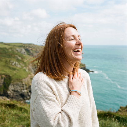 A woman laughing in the wind on a clifftop, wearing a powder blue cuff