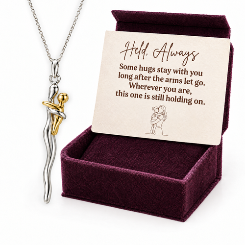 The silver and gold hug necklace in front of its plum velvet gift box with the Held, Always card