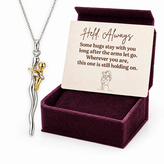 The silver and gold hug necklace in front of its plum velvet gift box with the Held, Always card