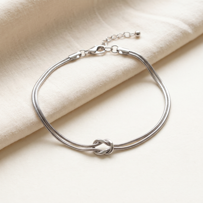 The silver Forever Knot bracelet open on cream cotton