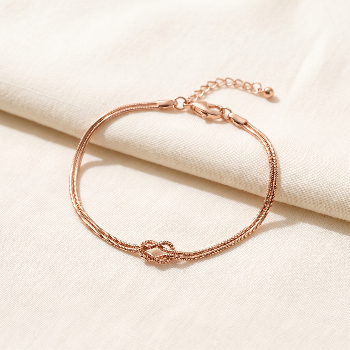 The rose gold Forever Knot bracelet open on cream cotton