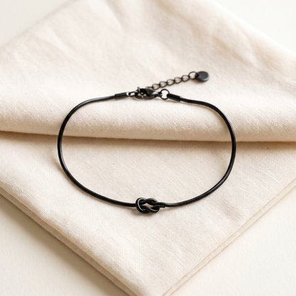 The matte black Forever Knot bracelet open on cream cotton