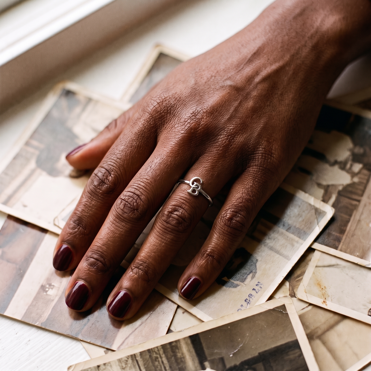 The silver interlocking initial ring worn on a hand resting on old family photographs