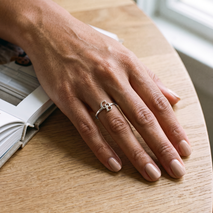 The silver interlocking initial ring worn on a hand resting on an oak table beside a photo album