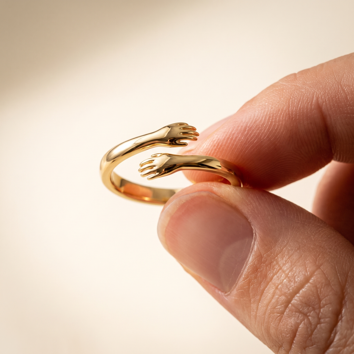 Fingertips holding the dainty gold hug ring showing the two hugging hands