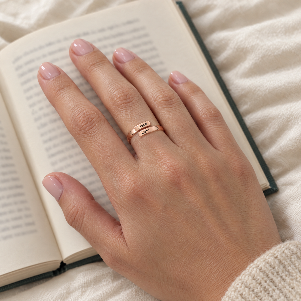 The rose gold ring worn on a hand resting on an open book