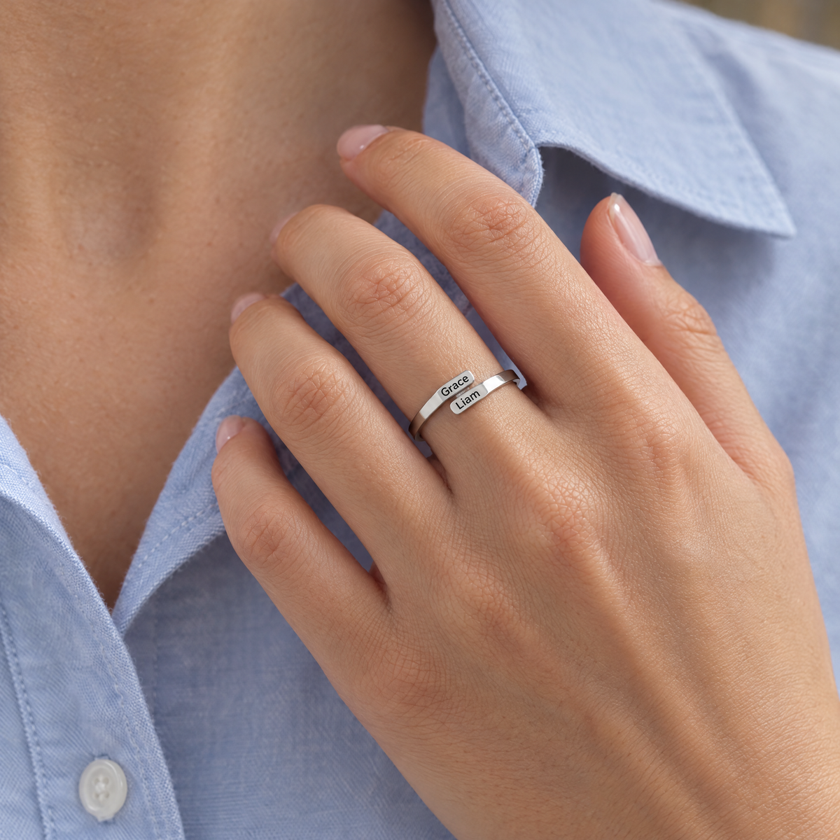 The silver ring worn on a hand resting on a blue shirt collar