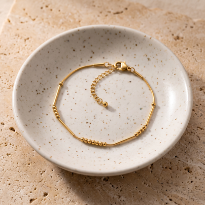 The gold Morse code chain bracelet fastened in a small ceramic dish