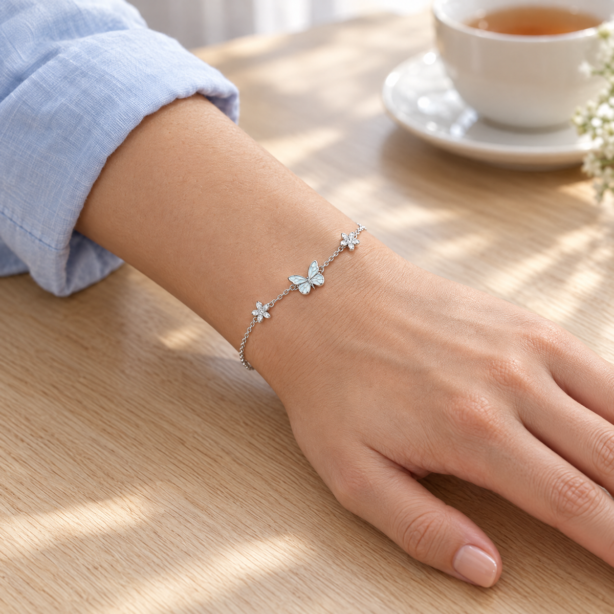 The butterfly bracelet worn with a rolled pale blue shirt sleeve, hand resting on an oak table