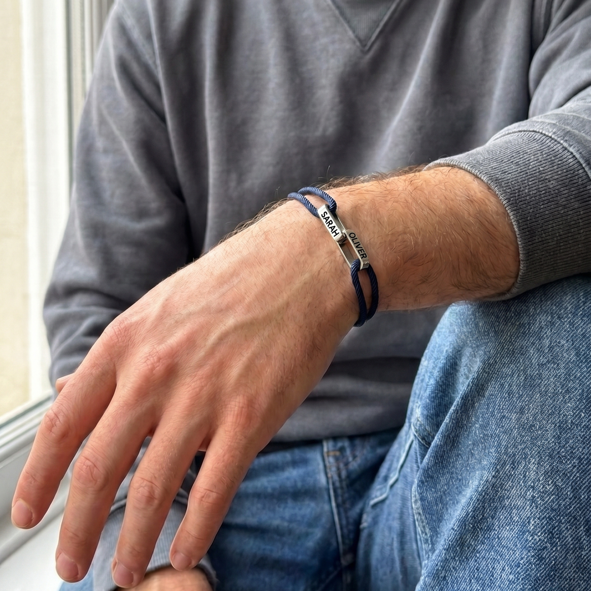 The bracelet worn by a man in a grey sweatshirt, the two linked names on top of his wrist